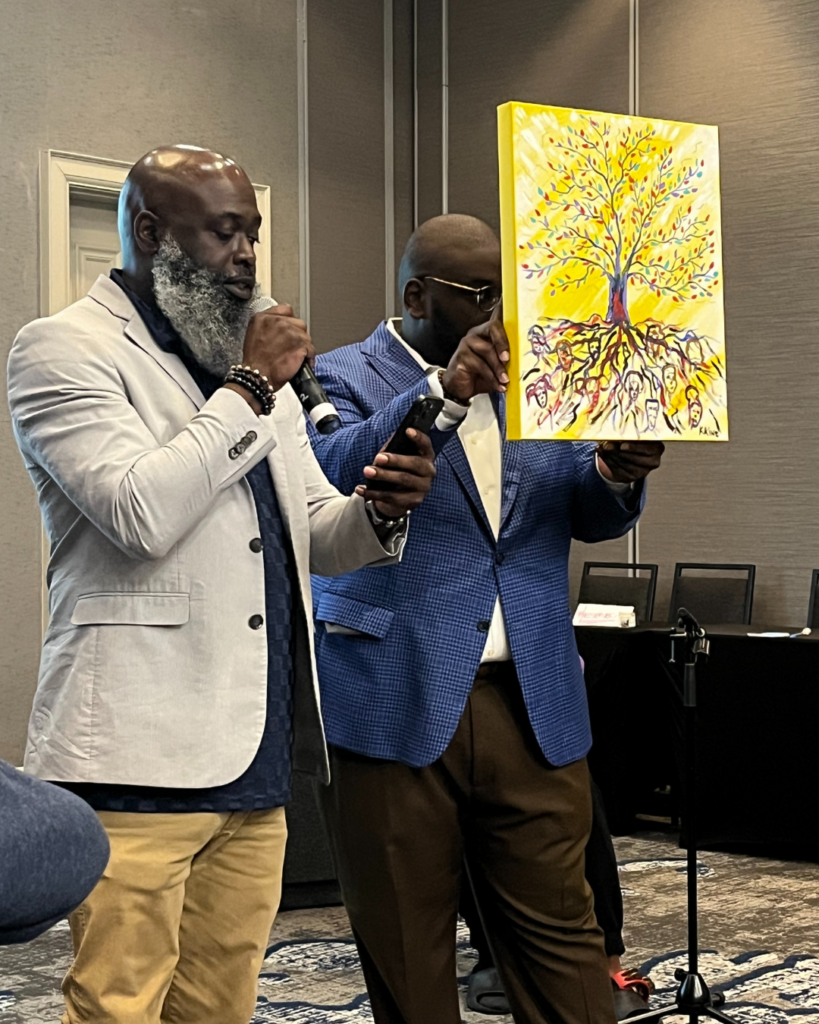 Pastor Richard Williams of the Metropolitan United Methodist Church in Montgomery and an African-American painter welcome guests. The painting features a tree on a yellow background, and faces are found in the roots.