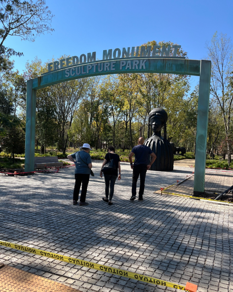 People walk toward the Freedom Monument Sculpture Park. A large statue of an African-American woman greets them.